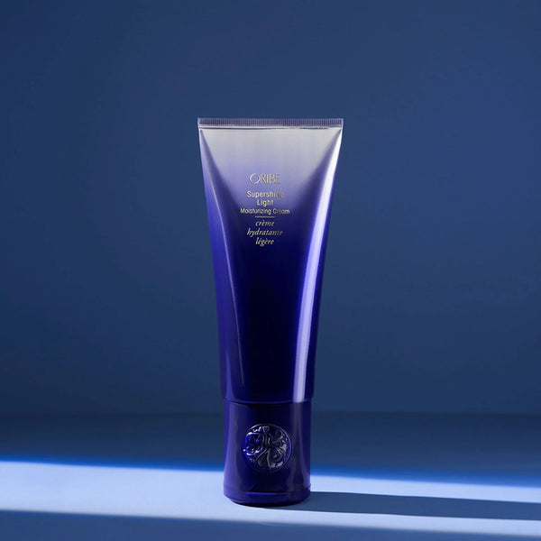 Oribe Supershine Light Moisturizing Cream in soft pearl white tube with gold detailing — a lightweight, leave-in styling cream that smooths frizz, adds shine, and hydrates fine to medium hair without weighing it down.