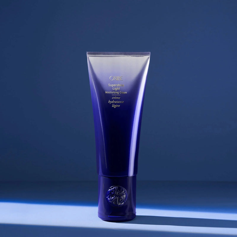 Oribe Supershine Light Moisturizing Cream in soft pearl white tube with gold detailing — a lightweight, leave-in styling cream that smooths frizz, adds shine, and hydrates fine to medium hair without weighing it down.
