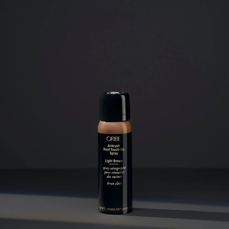 Oribe Airbrush Root Touch‑Up Spray in Light Brown – slim black aerosol can with brown sprayed top, sleek gold logo, and quick-drying microfine pigment formula for root coverage.